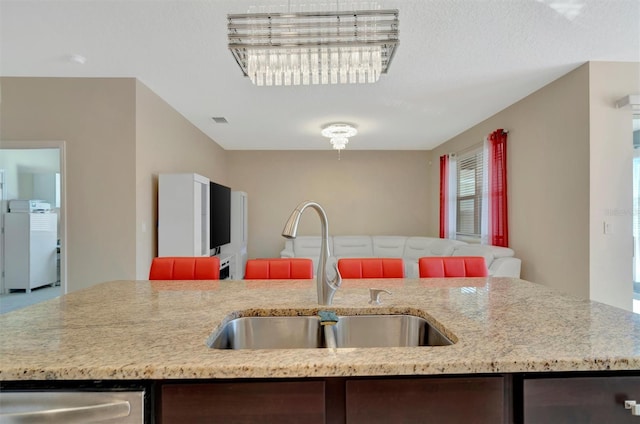 kitchen with a sink, stainless steel dishwasher, refrigerator, open floor plan, and light stone countertops