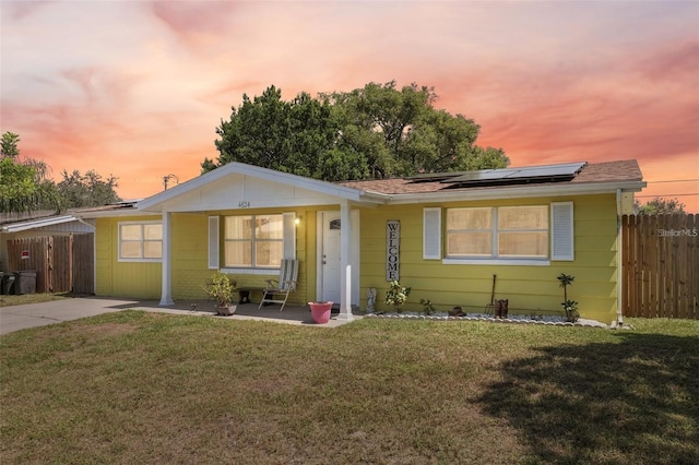 ranch-style house featuring a lawn, fence, and roof mounted solar panels