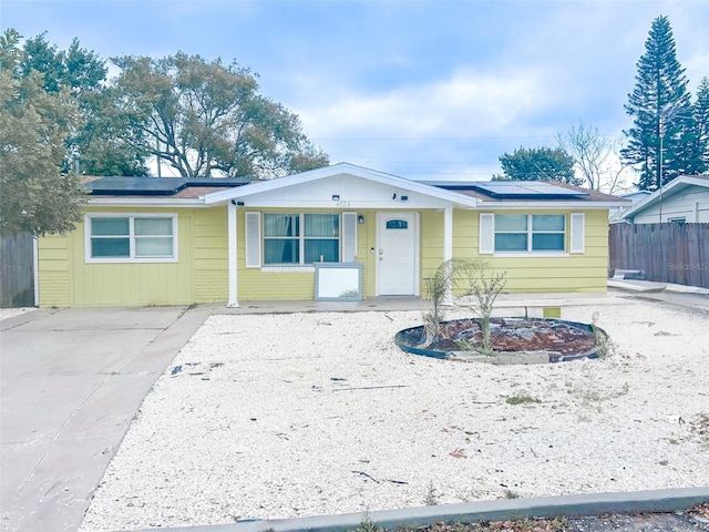 ranch-style house with roof mounted solar panels, brick siding, driveway, and fence