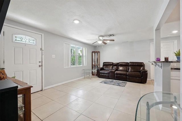 living area featuring light tile patterned floors, ceiling fan, visible vents, and a textured ceiling