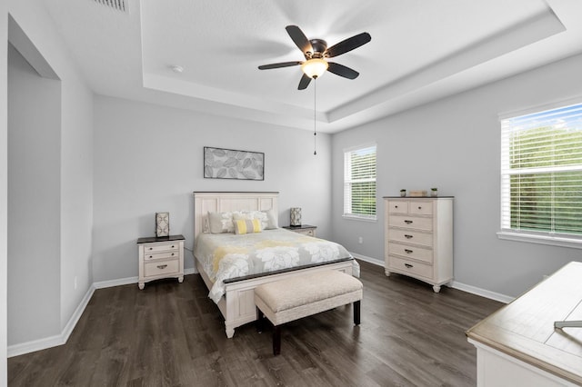 bedroom featuring a tray ceiling, baseboards, and dark wood-type flooring