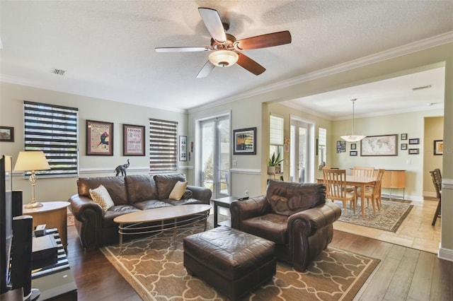 living room with a ceiling fan, wood-type flooring, ornamental molding, and a textured ceiling