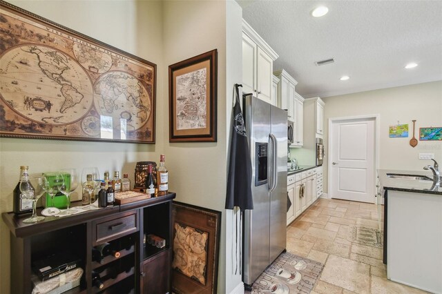 kitchen with stone tile floors, white cabinets, stainless steel fridge with ice dispenser, a sink, and recessed lighting