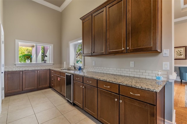 kitchen featuring light tile patterned floors, a sink, dark brown cabinets, light stone countertops, and crown molding