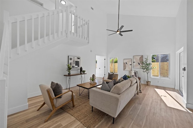 living room featuring ceiling fan, a high ceiling, baseboards, and wood finished floors