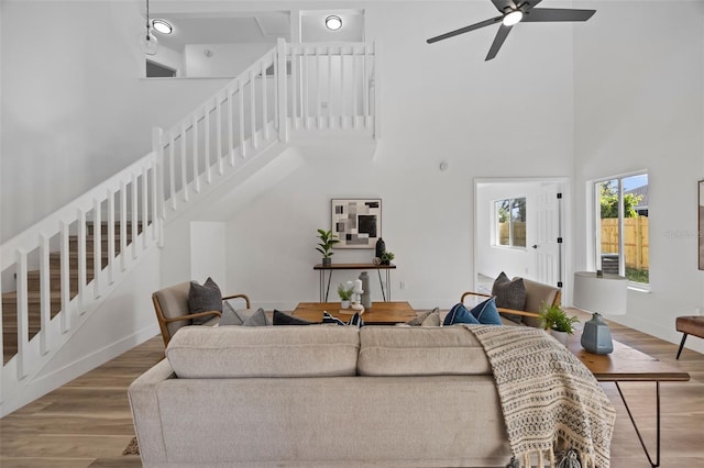 living room featuring baseboards, a ceiling fan, stairway, wood finished floors, and a high ceiling