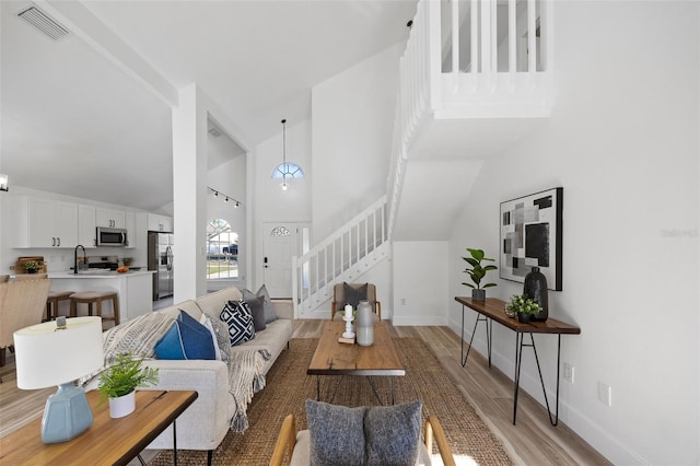 living room featuring high vaulted ceiling, visible vents, baseboards, stairs, and light wood-type flooring