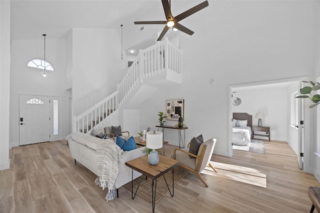 living area with baseboards, a towering ceiling, ceiling fan, wood finished floors, and stairs