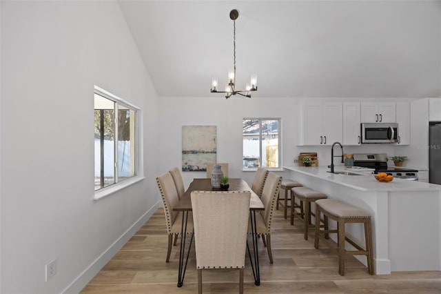 dining area with an inviting chandelier, light wood-style flooring, baseboards, and vaulted ceiling