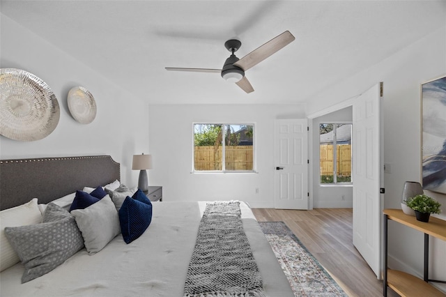 bedroom featuring ceiling fan, multiple windows, baseboards, and wood finished floors