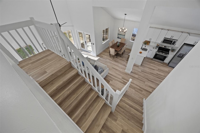 stairs with high vaulted ceiling, wood finished floors, and an inviting chandelier