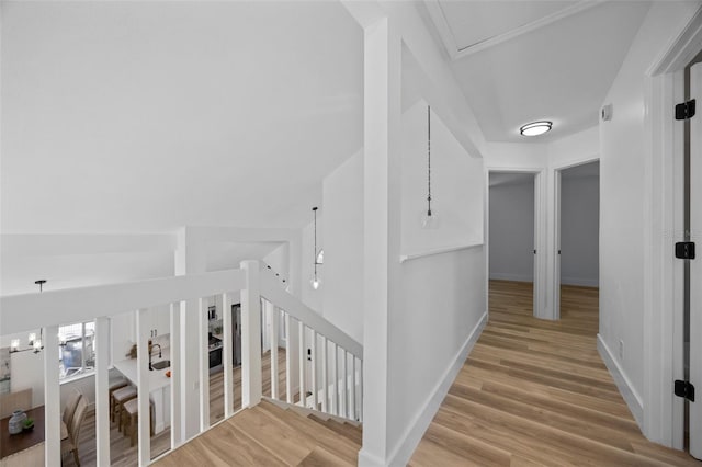 corridor featuring a chandelier, baseboards, light wood finished floors, and an upstairs landing