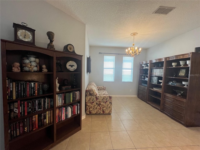 living area featuring light tile patterned floors, visible vents, a textured ceiling, a chandelier, and baseboards