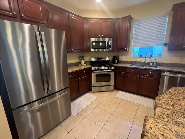 kitchen with light tile patterned floors, stainless steel appliances, dark stone countertops, and a sink