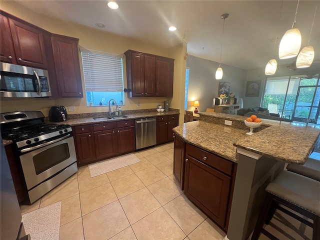 kitchen featuring light tile patterned floors, stainless steel appliances, a sink, a kitchen breakfast bar, and dark stone countertops