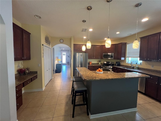 kitchen with arched walkways, stainless steel appliances, light tile patterned floors, and a sink