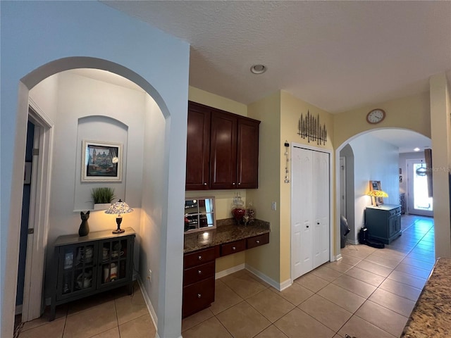 hall featuring a textured ceiling, baseboards, and light tile patterned floors