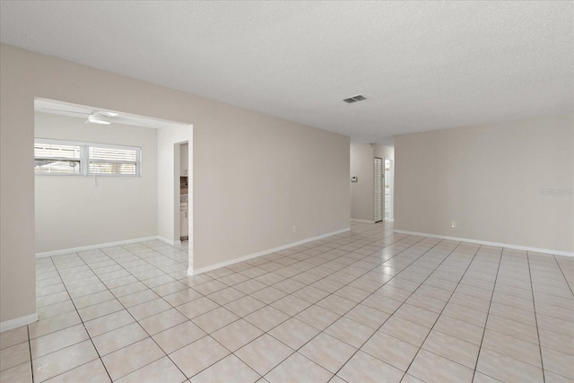 empty room featuring a textured ceiling, light tile patterned flooring, visible vents, and baseboards