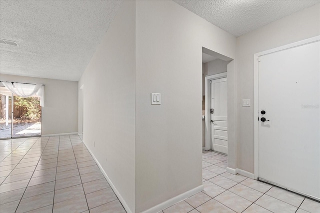 corridor with light tile patterned floors, baseboards, visible vents, and a textured ceiling