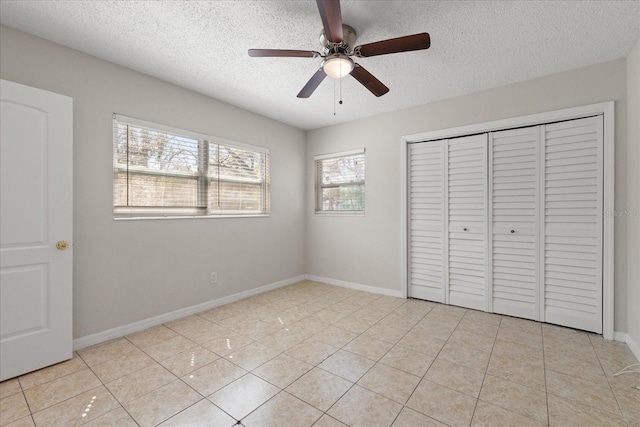 unfurnished bedroom featuring light tile patterned floors, a textured ceiling, baseboards, and a closet