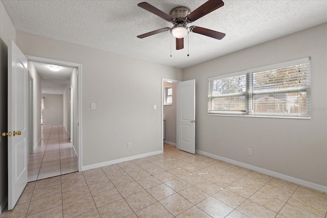 unfurnished bedroom with light tile patterned floors, ceiling fan, baseboards, and a textured ceiling