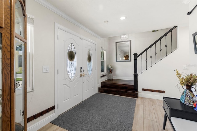 foyer entrance with ornamental molding, light wood-type flooring, baseboards, and stairs