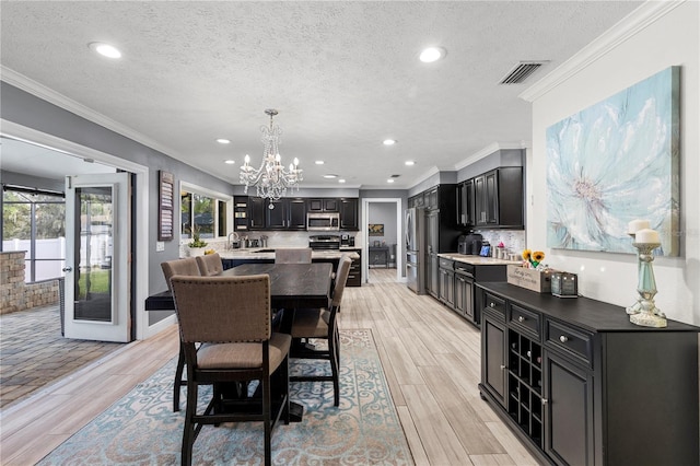 dining area with an inviting chandelier, light wood-type flooring, visible vents, and crown molding