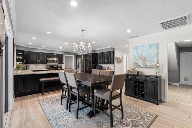 dining area with a textured ceiling, light wood finished floors, visible vents, and crown molding