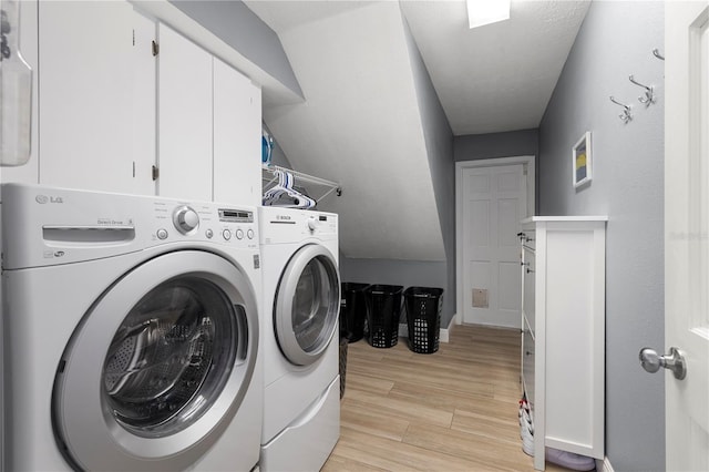 laundry area with light wood-type flooring, washing machine and dryer, and cabinet space