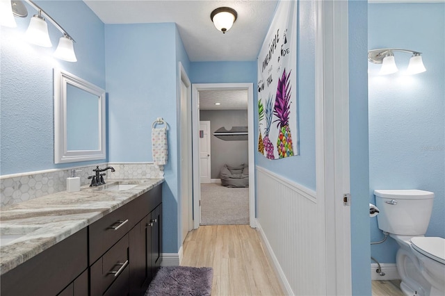 full bath featuring toilet, a wainscoted wall, wood finished floors, and vanity