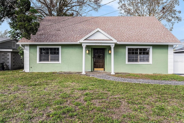 view of front of home with a front yard, roof with shingles, and stucco siding