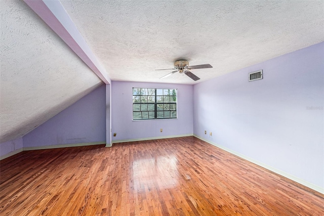 additional living space featuring baseboards, visible vents, wood-type flooring, vaulted ceiling, and a textured ceiling