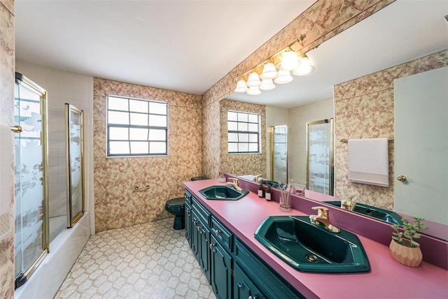 full bath featuring double vanity, a sink, toilet, and bath / shower combo with glass door