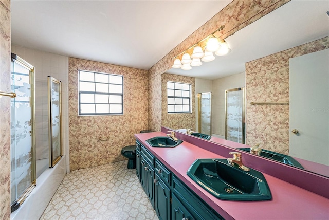 full bathroom with double vanity, a sink, toilet, and bath / shower combo with glass door