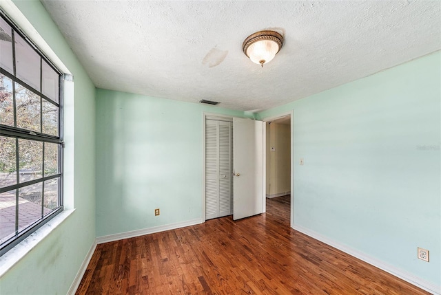 empty room featuring a textured ceiling, wood finished floors, visible vents, and baseboards