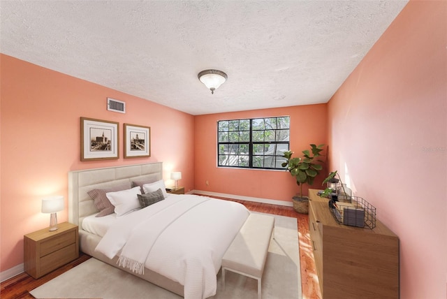 bedroom featuring baseboards, a textured ceiling, visible vents, and wood finished floors