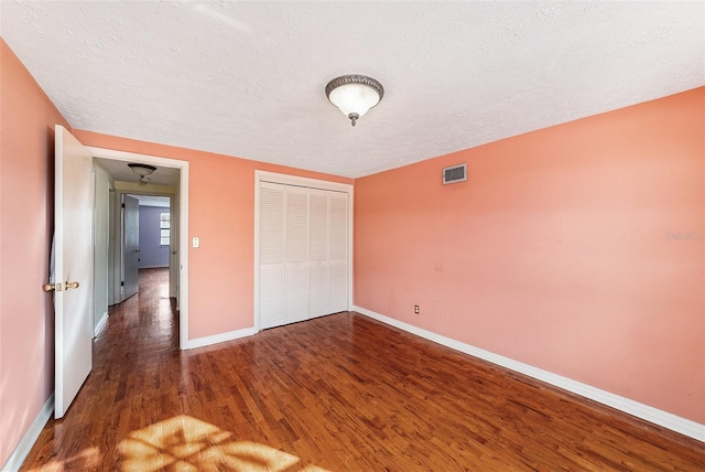 unfurnished bedroom featuring baseboards, visible vents, wood finished floors, a textured ceiling, and a closet