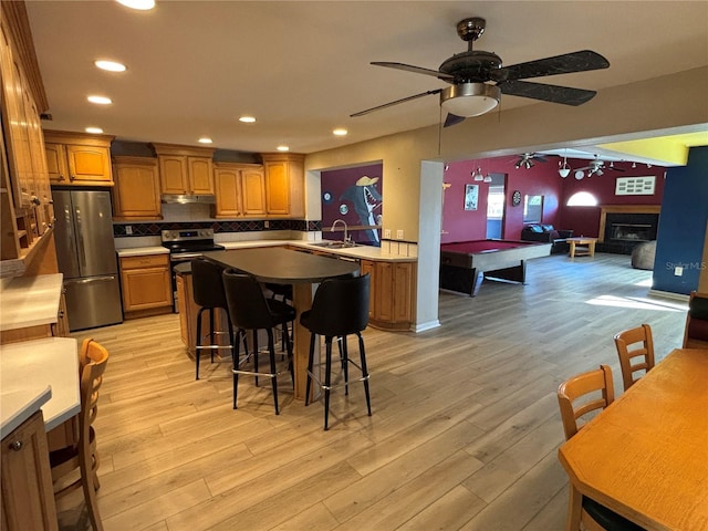 kitchen with brown cabinets, light wood finished floors, appliances with stainless steel finishes, open floor plan, and a sink