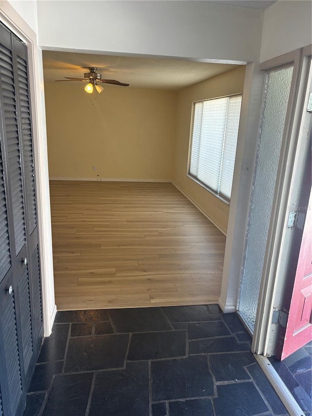 interior space with baseboards, ceiling fan, and stone tile floors