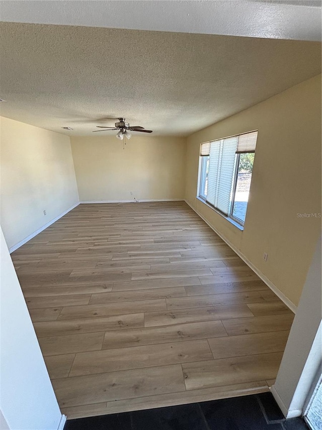 empty room with light wood-type flooring, ceiling fan, baseboards, and a textured ceiling