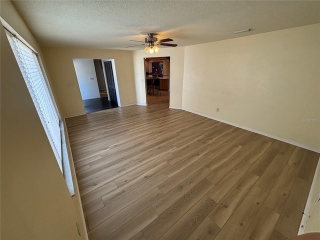 spare room featuring baseboards, visible vents, ceiling fan, wood finished floors, and a textured ceiling