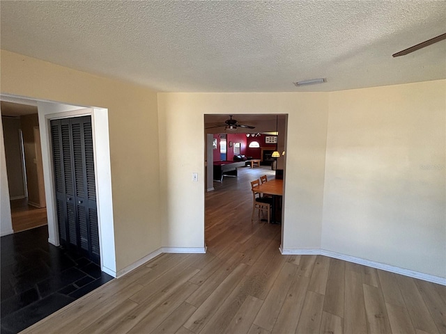 interior space featuring a ceiling fan, visible vents, baseboards, and wood finished floors