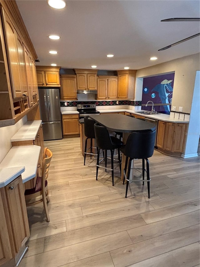 kitchen with appliances with stainless steel finishes, brown cabinetry, a sink, and light wood-style flooring