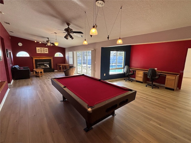 game room featuring a textured ceiling, pool table, vaulted ceiling, light wood-type flooring, and a glass covered fireplace