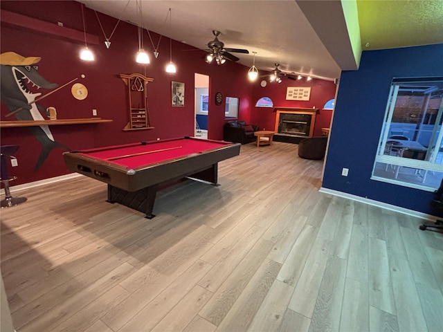 playroom featuring a fireplace with raised hearth, a ceiling fan, vaulted ceiling, wood finished floors, and baseboards