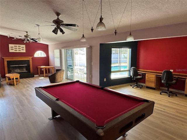 playroom with lofted ceiling, a fireplace with raised hearth, light wood-style floors, a ceiling fan, and a textured ceiling