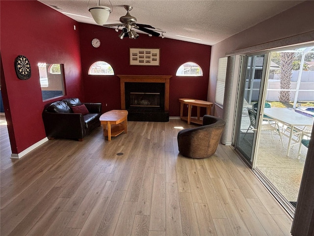 living area with baseboards, a fireplace with raised hearth, wood finished floors, vaulted ceiling, and a textured ceiling