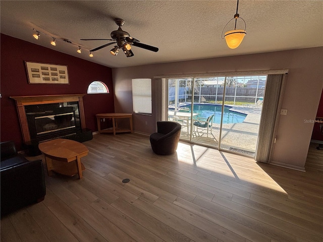 living area with lofted ceiling, a high end fireplace, a textured ceiling, track lighting, and wood finished floors