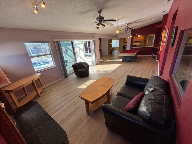 living room with light wood-style floors, vaulted ceiling, a textured ceiling, and track lighting