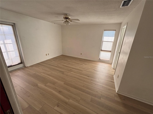 empty room featuring a textured ceiling, wood finished floors, visible vents, baseboards, and a ceiling fan